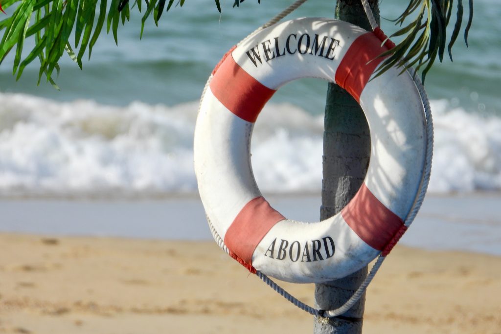 Photo of beach with lifebuoy that says "Welcome Aboard" Photo by Nick Fewings on Unsplash